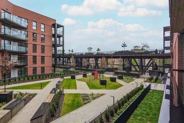 A modern urban courtyard with a pedestrian bridge, surrounded by multi-story buildings with balconies.
