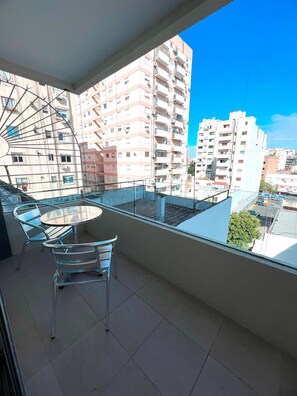 A balcony with a table and chairs, overlooking a cityscape with multiple buildings.
