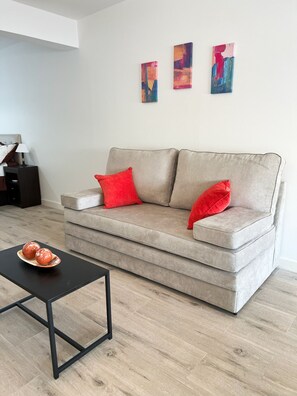 Un salon avec un canapé gris, deux coussins rouges, une table basse noire et une assiette contenant deux objets rouges.