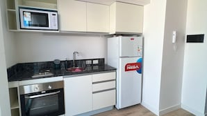 A compact kitchen with a microwave, oven, refrigerator, and a sink. - Brand new studio in Almagro with rooftop terrace, bathtub and balcony | Hospital Italiano, audiovisual hub & Av. Corrientes (Buenos Aires)