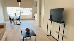 A modern living room with a dining area, a flat-screen TV on a stand, and a bowl of fruit on a small table. - Brand new studio in Almagro with rooftop terrace, bathtub and balcony | Hospital Italiano, audiovisual hub & Av. Corrientes (Buenos Aires)