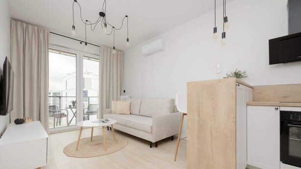 Una sala de estar moderna con sofá, una mesita, una cocina con estufa y un amplio ventanal con cortinas.