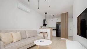 Una sala de estar moderna con un sofá, una mesa redonda de centro y una cocina al fondo.