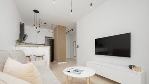 Una sala de estar moderna con un sofá blanco, una mesa de centro redonda y un televisor de pantalla plana montado en la pared.