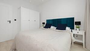 Un dormitorio con una cama grande, un armario blanco, una mesita de noche con lámpara y un cabecero color aguamarina.