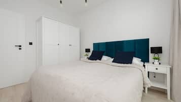 A bedroom with a large bed, a white wardrobe, a nightstand with a lamp, and a teal headboard.