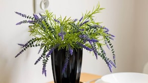A dining table with two white plates, a black vase with purple flowers, and a black placemat.