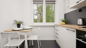 A compact kitchen with white cabinetry, a wooden countertop, a window with a view of trees, and a small table with chairs.