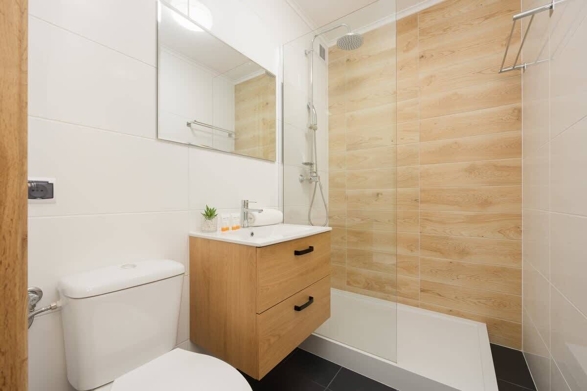 A modern bathroom with a wooden shower enclosure, a white toilet, and a vanity with drawers.