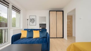 A modern living room with a blue sofa, a yellow cushion, a black coffee table, and a wooden wardrobe.