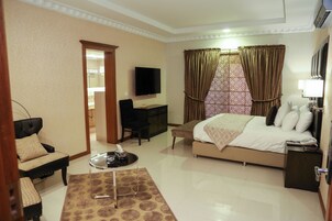 A hotel room with a bed, a desk, a TV, and a seating area.