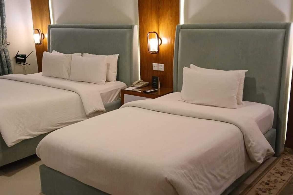 A hotel room with two beds, each with a headboard and bedside lamps.