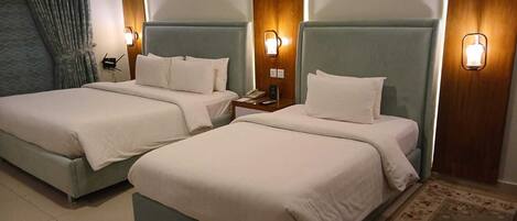 A hotel room with two beds, each with a headboard and bedside lamps.