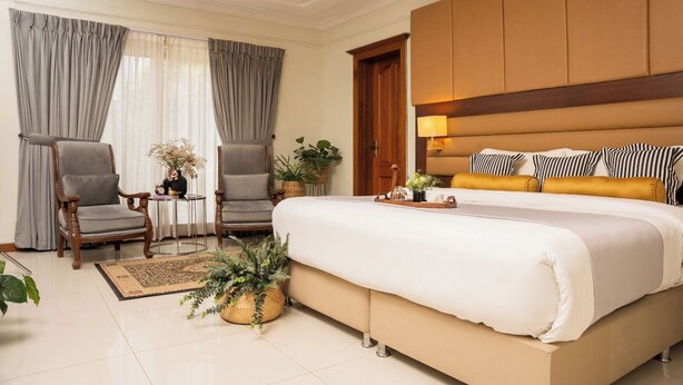 A hotel room with a large bed, two armchairs, a small table, and a potted plant. - Grace Guest House (Islamabad)