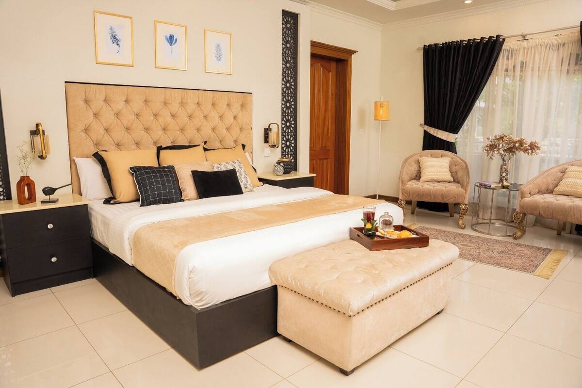 A spacious bedroom with a large bed, two bedside tables, a nightstand, a sofa, and a small round table.