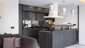 Une cuisine moderne avec des meubles de couleur sombre, un îlot central et des luminaires suspendus.