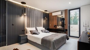 Une chambre moderne avec un grand lit, des tables de chevet, un miroir et une vue sur l’extérieur grâce à une porte vitrée.