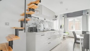 A modern kitchen with a central island, white cabinetry, and a wooden staircase.