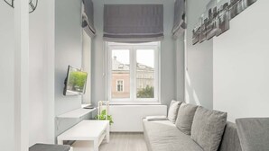 A modern living room with a grey sofa, a white table, and a window with a view of buildings.