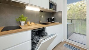 Una cocina moderna con armarios blancos, encimera de madera, lavavajillas integrado, cafetera y vistas al exterior.