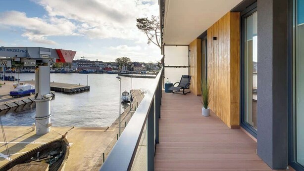 Un balcón con vista a un puerto deportivo, piso de madera y una planta en maceta.