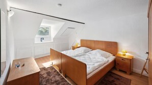 A bedroom with a sloped ceiling, a bed with wooden headboard, two bedside tables with lamps, a small window, and a radiator. - 1 bedroom nice apartment in Kaub (Kaub)