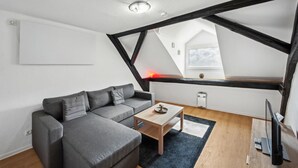 A modern loft bedroom with exposed wooden beams, a gray sofa, a wooden coffee table, and a view of the sky through a skylight. - 1 bedroom nice apartment in Kaub (Kaub)