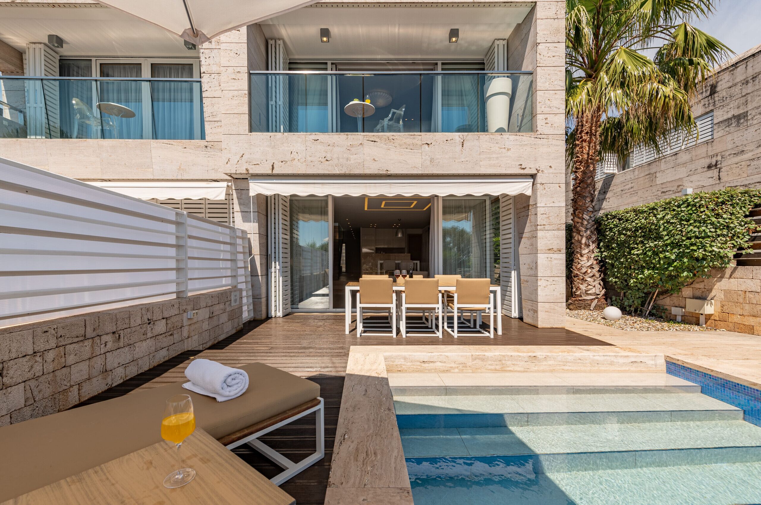 Un espace piscine extérieur moderne, avec un fauteuil de relaxation, un verre à portée de main et une table à manger avec des chaises.