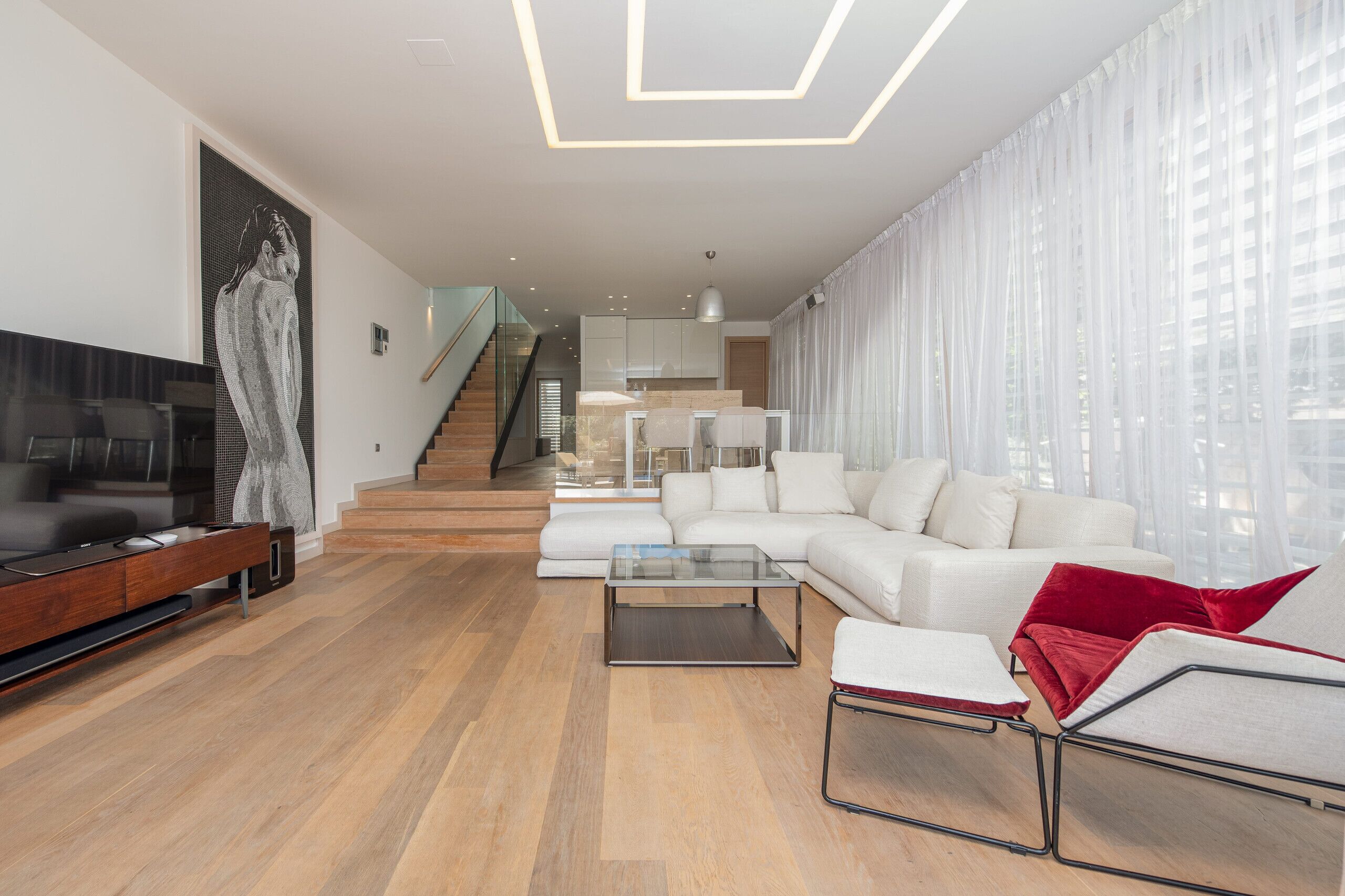 A modern living room with a sofa, coffee table, and TV. A staircase leads to an upper level.