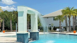 A swimming pool with a water feature, surrounded by palm trees and a building in the background. - 8BR Pool & Arcade – Enchanted Escape Retreat (Kissimmee)