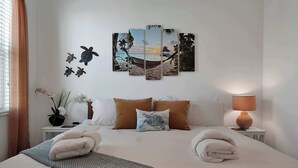 A neatly made bed with towels, a wall art of a beach scene, and a lamp on a bedside table. - 8BR Pool & Arcade – Enchanted Escape Retreat (Kissimmee)