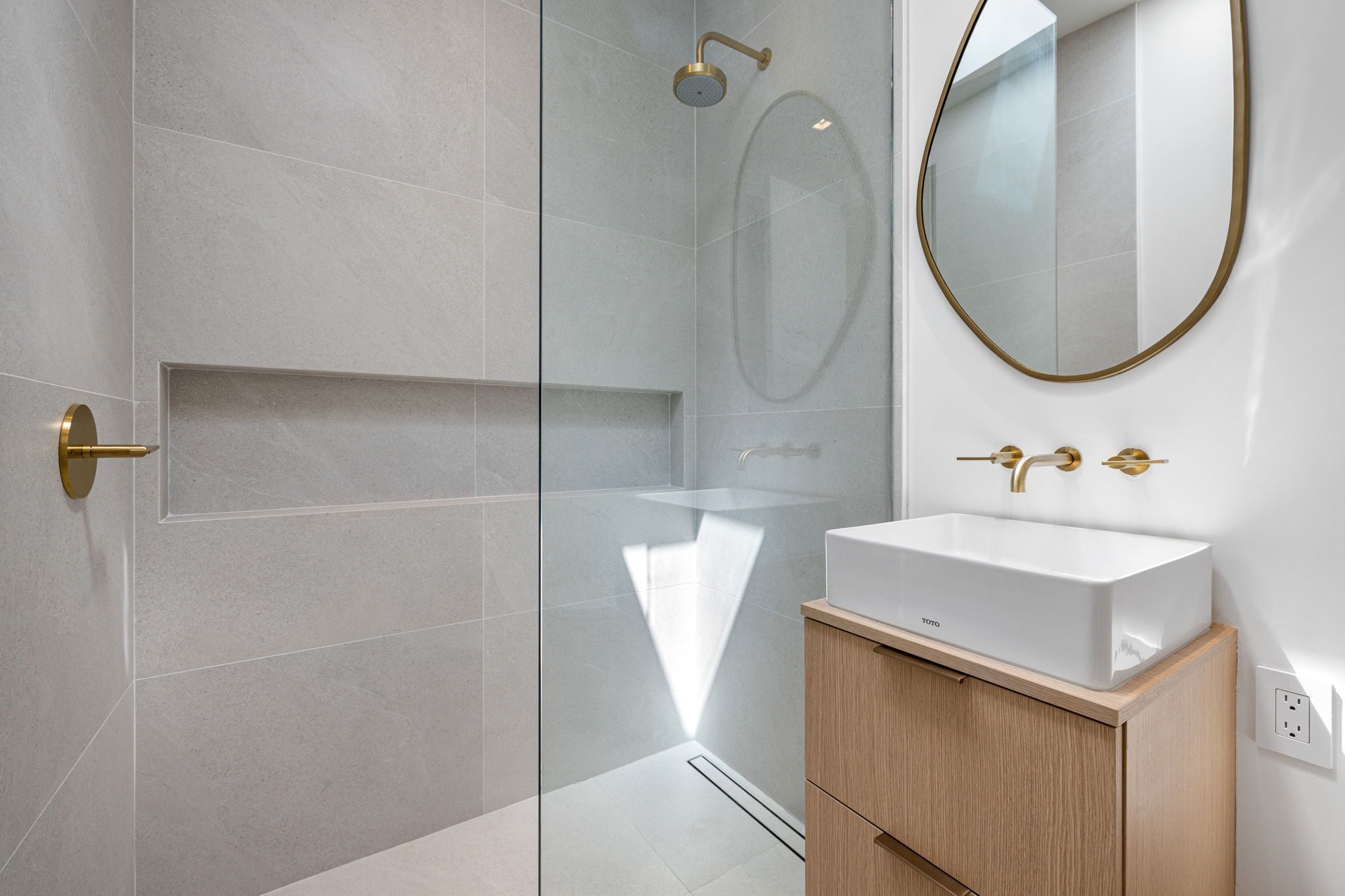 Een moderne badkamer met een douchecabine van glas, een witte wastafel en een houten opbergmeubel.