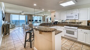 A modern kitchen with a large island, white cabinetry, and a view to the outside. - Deluxe Beachfront Condo (Panama City Beach)