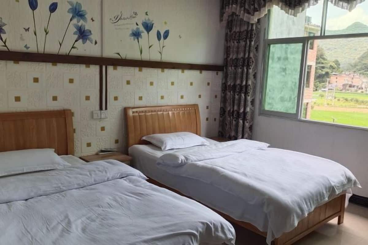 Una habitación con dos camas, cabecero de madera, pared con diseño floral y ventana con vistas a la vegetación.