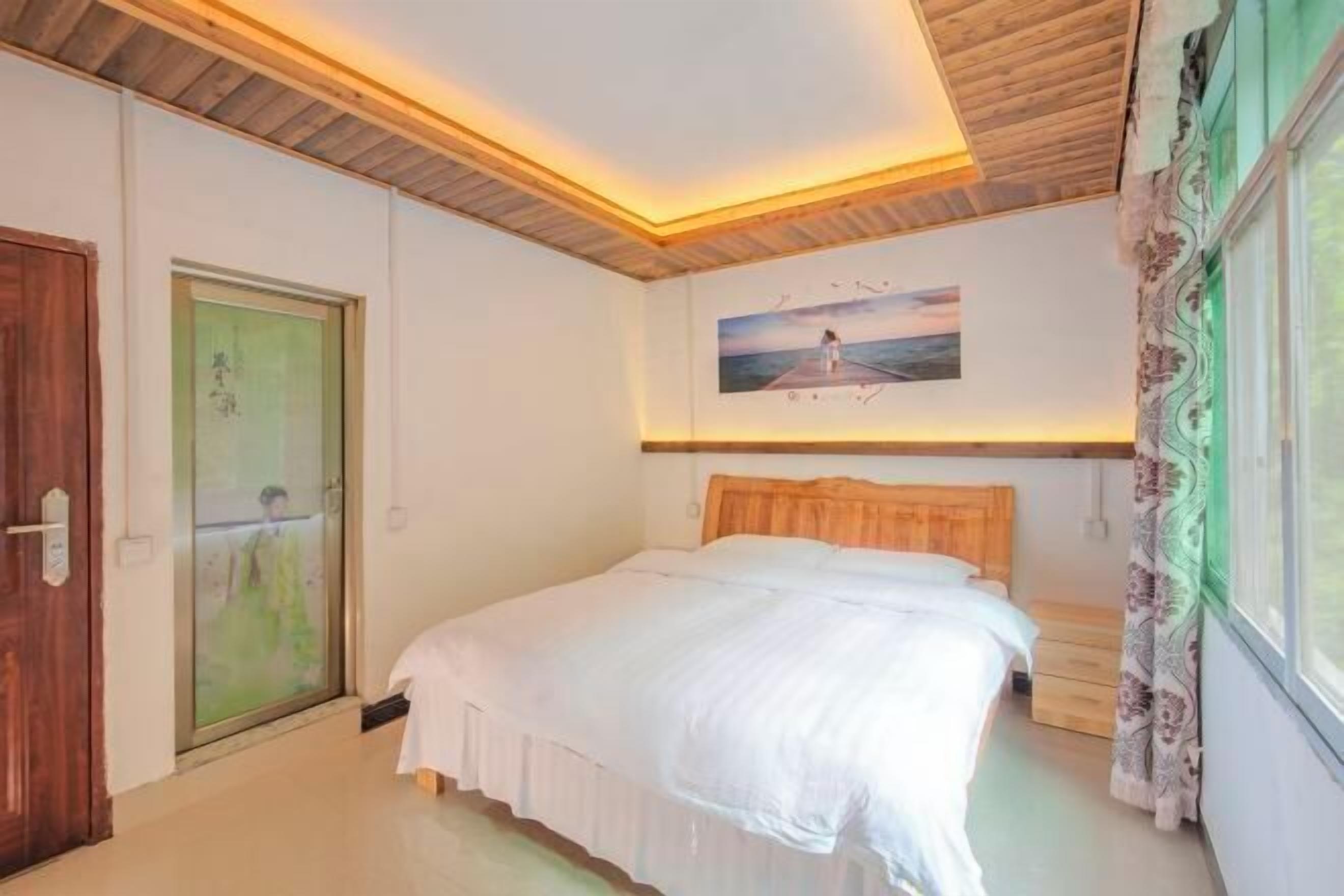A bedroom with a wooden ceiling, a bed with white bedding, a painting of a pier, and a window with curtains.