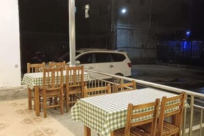 A balcony with wooden chairs and tables, a white car parked outside, and a railing.