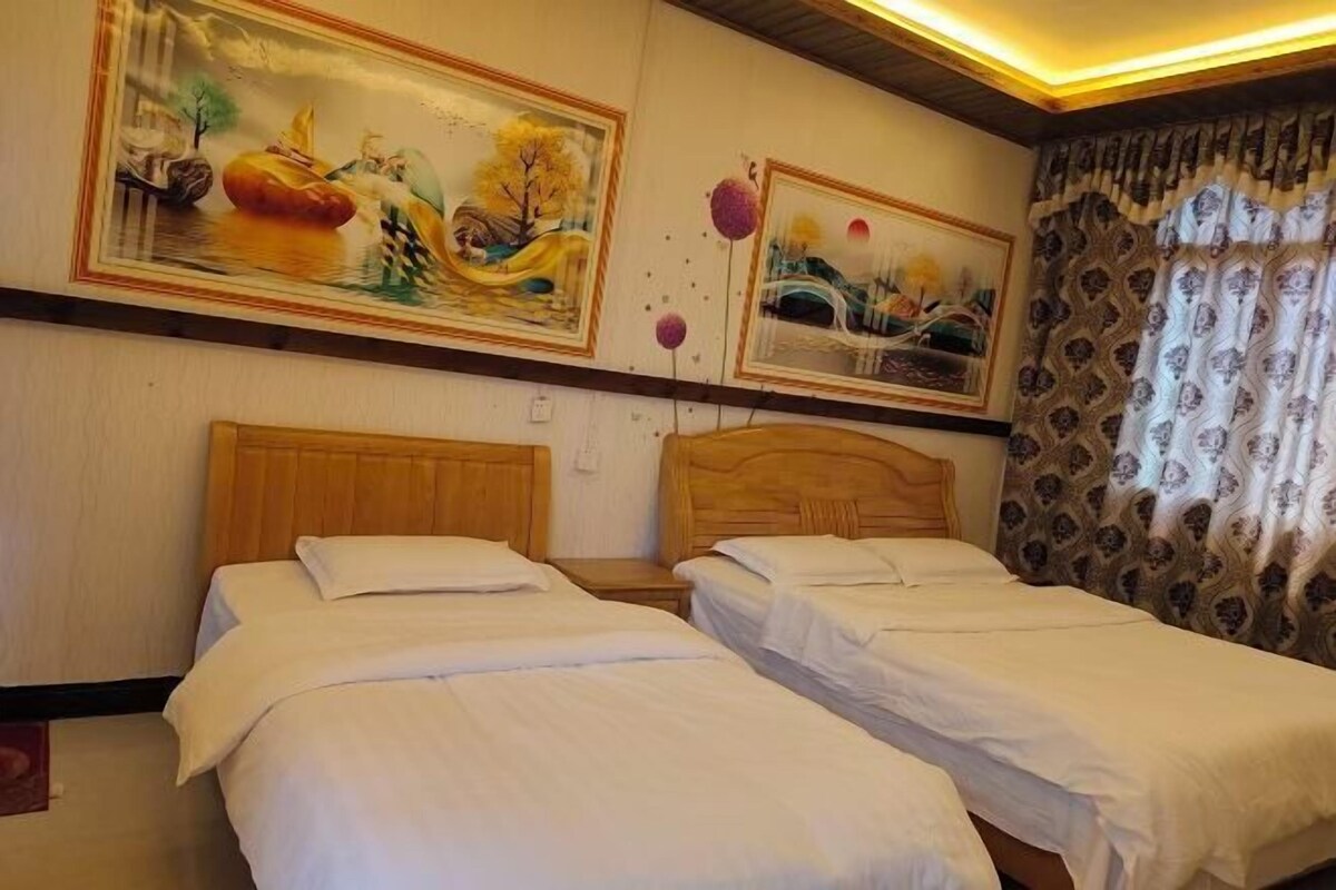 A hotel room with two single beds, wooden headboards, and two large landscape paintings on the wall.