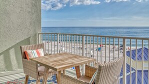 A balcony with wicker furniture, a wooden table, and a view of the beach and ocean.