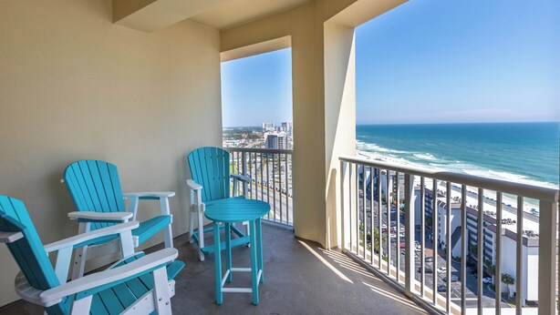Ein Balkon mit türkisfarbenen Adirondack-Stühlen und Blick aufs Meer.