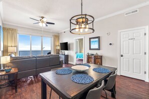A dining area with a wooden table, blue placemats, and a ceiling fan. - Newly Renovated Upscale Beachfront Condo (Panama City Beach)