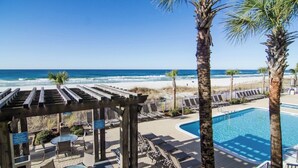 A beachside pool area with lounge chairs, a wooden pergola, and a view of the ocean. - Big Beachfront Balcony for Parties of 7 with a set of beach chairs included! (Panama City Beach)