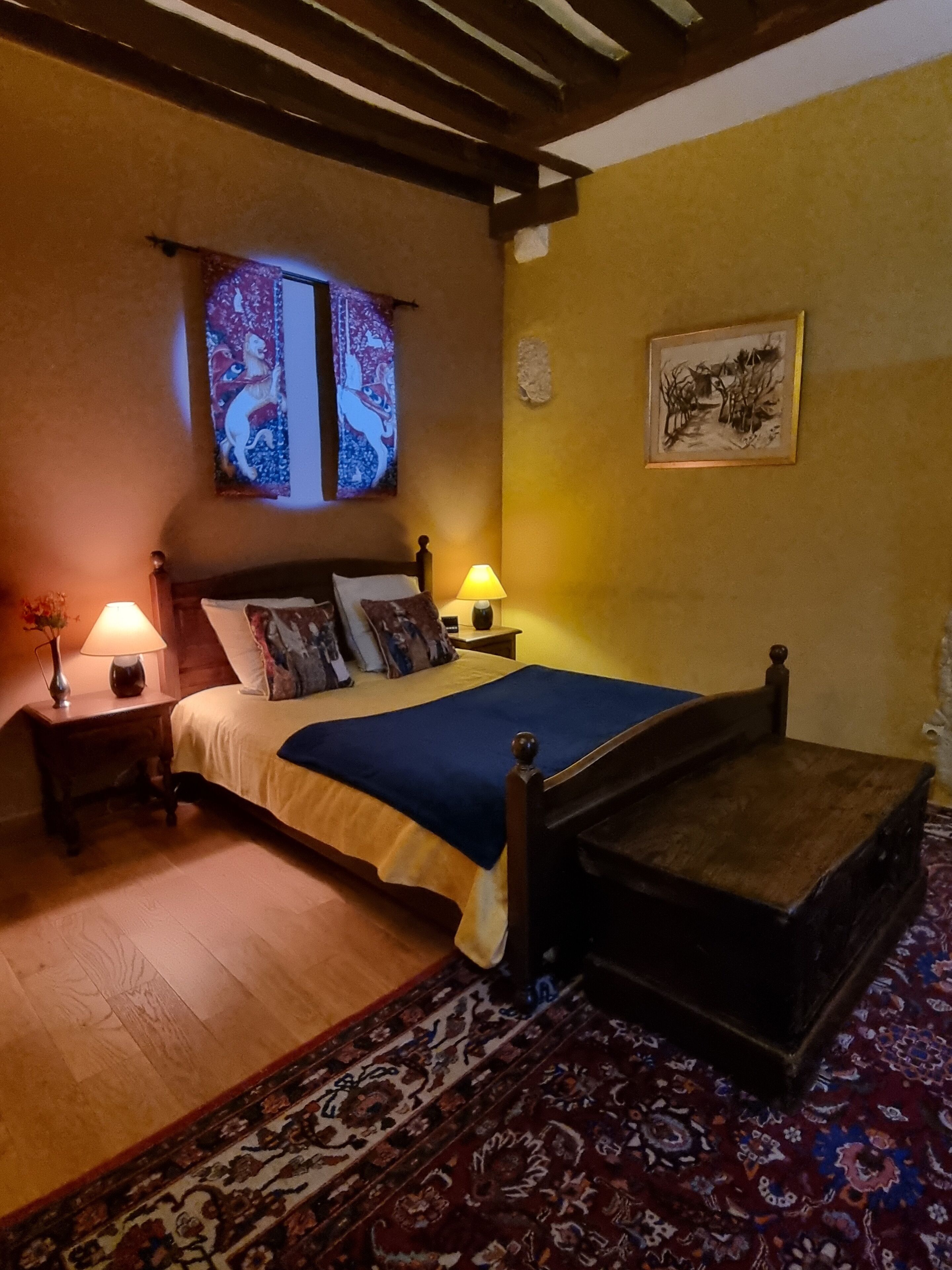 A bedroom with a wooden bed, two bedside lamps, a rug, and a painting on the wall.