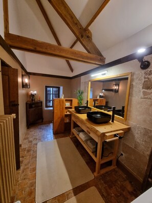 A rustic kitchen with wooden beams, a stone wall, and a large mirror.