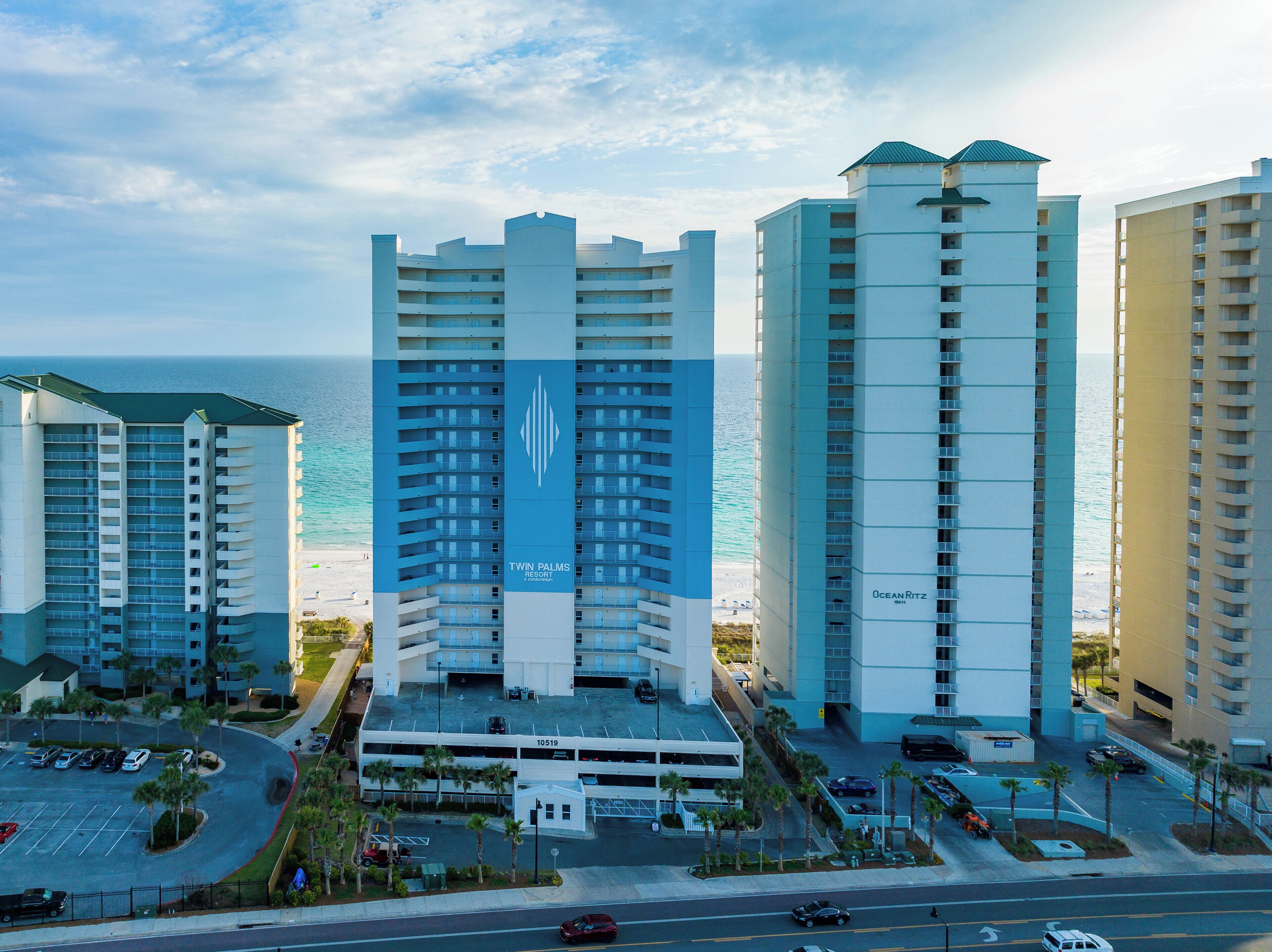 A high-rise hotel with a prominent logo, a parking garage, and a view of the beach.