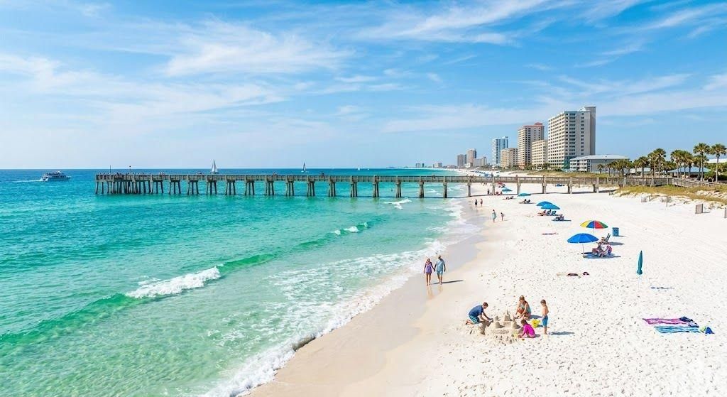 A beach with a pier extending into the water, people walking along the shore, and buildings in the background.