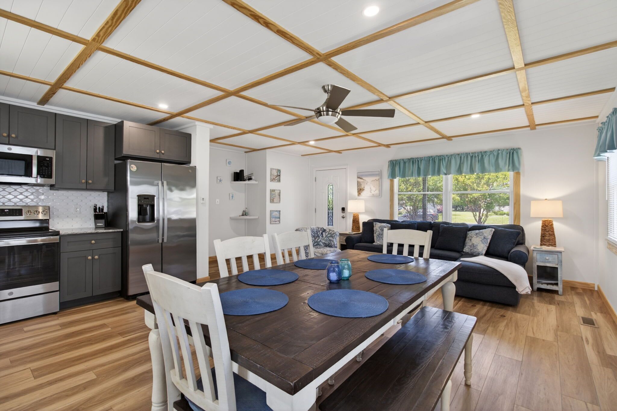 A modern kitchen with a dining area, wooden ceiling beams, and a ceiling fan.