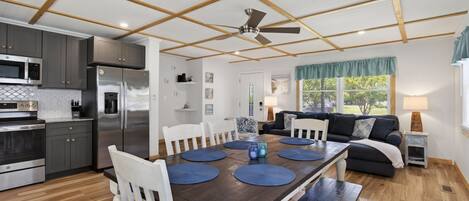 A modern kitchen with a dining area, wooden ceiling beams, and a ceiling fan.