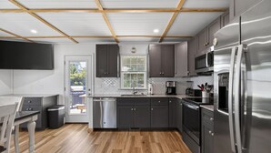 A modern kitchen with wooden flooring, stainless steel appliances, and a window with blinds. - Nautical Miles Home, Close to Park, Beach & Shops (Cape Charles)
