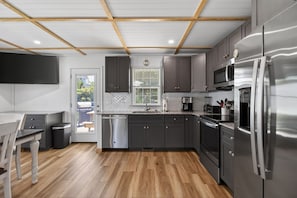 A modern kitchen with wooden flooring, stainless steel appliances, and a window with blinds.