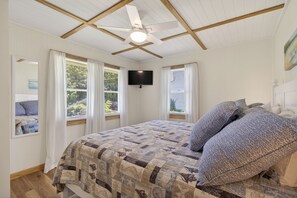 A bedroom with a bed, a ceiling fan, a TV, and windows with curtains.